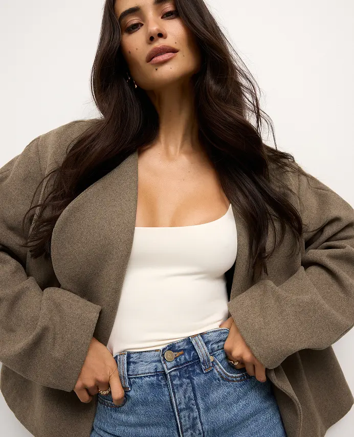 La mannequin porte un manteau en laine brun par-dessus une camisole blanche et un jean bleu.